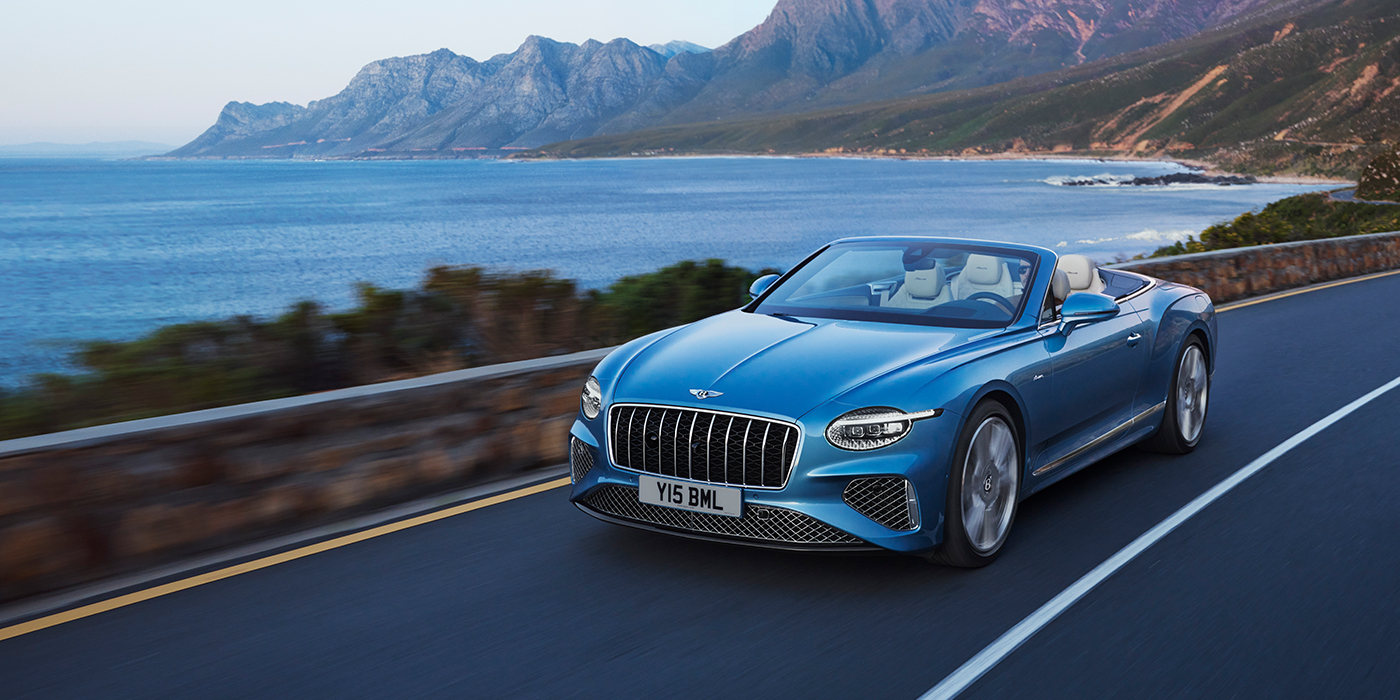 Bentley Antwerp New Bentley Continental GTC Azure convertible in Light Windsor blue paint with 22 inch Azure wheels and chrome grill, driving dynamically by the sea