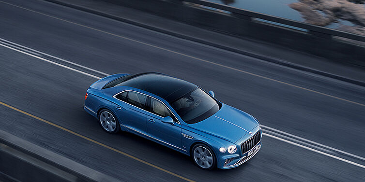 Bentley Antwerp New Bentley Flying Spur Azure sedan in Light windsor blue paint by Mulliner, with 22 inch Azure wheels seen from overhead driving dynamically on a country road