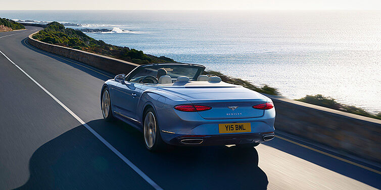 Bentley Antwerp New Bentley Continental GTC Azure convertible rear view in Light Windsor blue paint with 22 inch ten spoke wheels driving dynamically on an ocean road in the sunshine