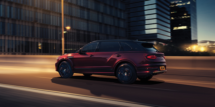 Bentley Antwerp Bentley Bentayga Extended Wheelbase Mulliner SUV in Cricket Ball red paint driving dynamically in city at night